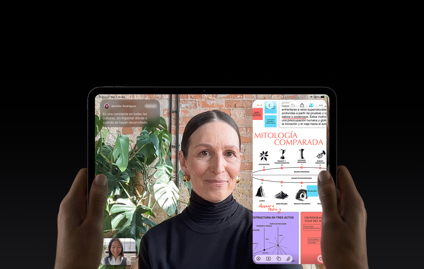 iPad Pro, parte frontal, en horizontal, negro espacial, esquinas redondeadas, pantalla de marco negro, manos sosteniendo los lados izquierdo y derecho, la pantalla muestra un conversación de FaceTime que se está traduciendo en vivo, del lado derecho hay una app educativa con una presentación de cuentos sobre heroísmo que contiene texto, diagramas y notas escritas a mano