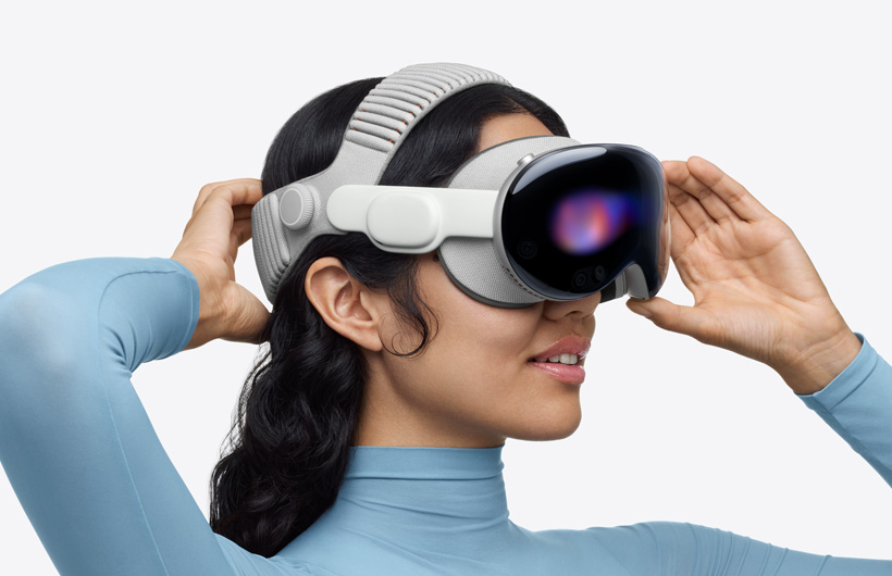 Person wearing Apple Vision Pro, assembled with Dual Knit Band, upper band spans across the top of the head, one hand placed on lower back band behind head, other hand placed on aluminum alloy frame
