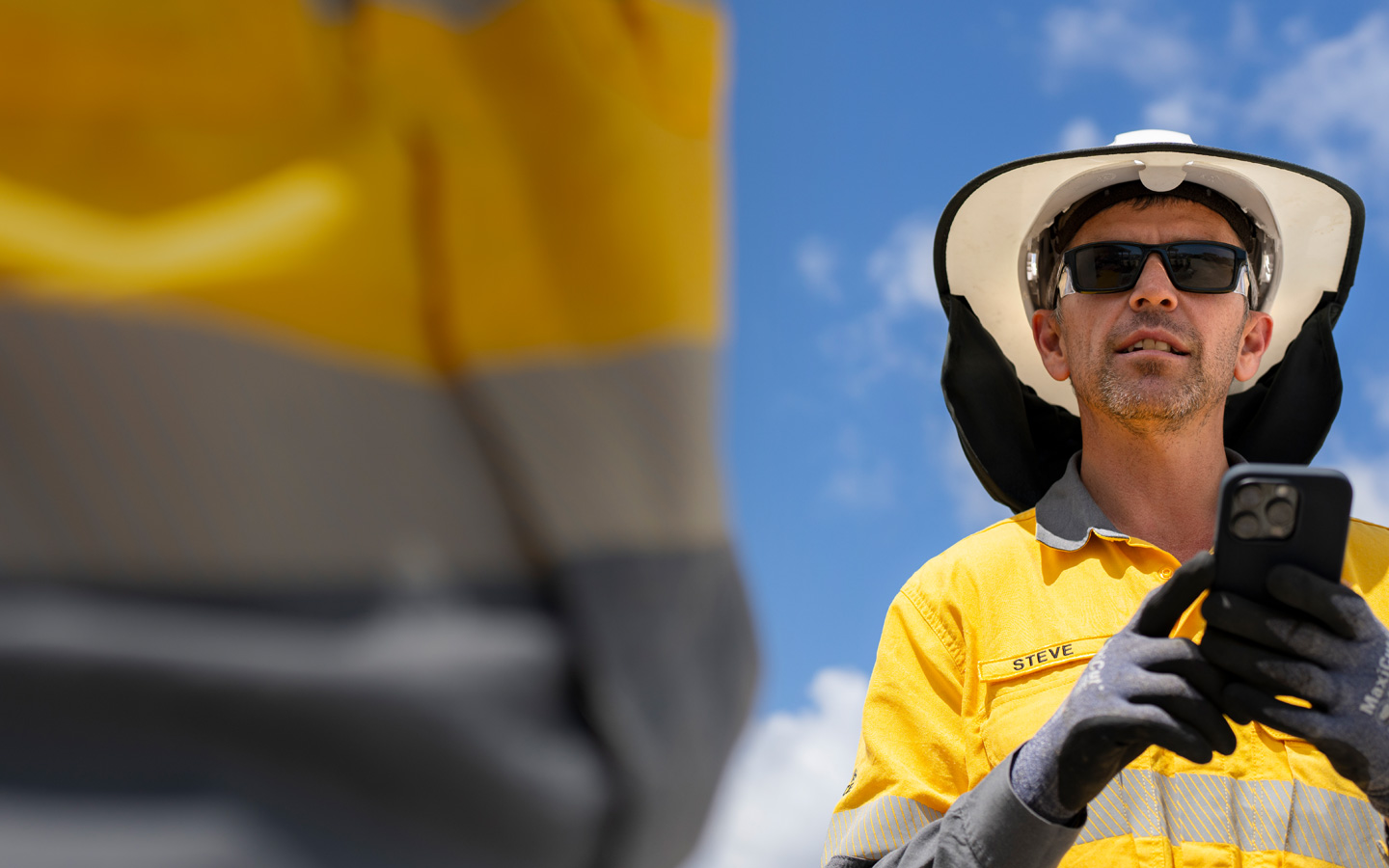 A field worker dressed in safety gear holds an iPhone while talking with a crew member