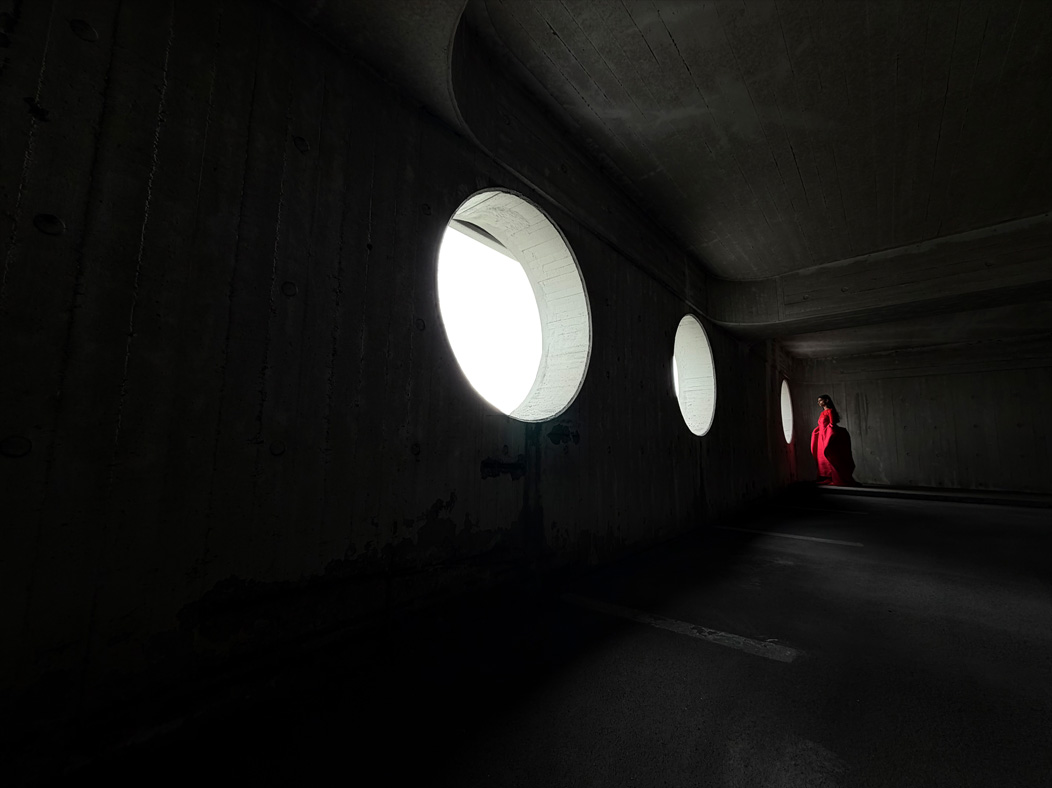 Tukšā telpā tiek fotografēta sieviete garā sarkanā kleitā. Lai demonstrētu pro kameru sistēmas iespējas, Photo aplikācijā tiek pārslēgti sekojoši fokusa attālumi: 200 mm, 100 mm, 48 mm, 35 mm, 28 mm, 13 mm un makro