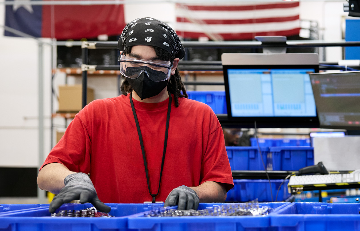 An employee wearing safety gloves, glasses and mask handles materials at a facility