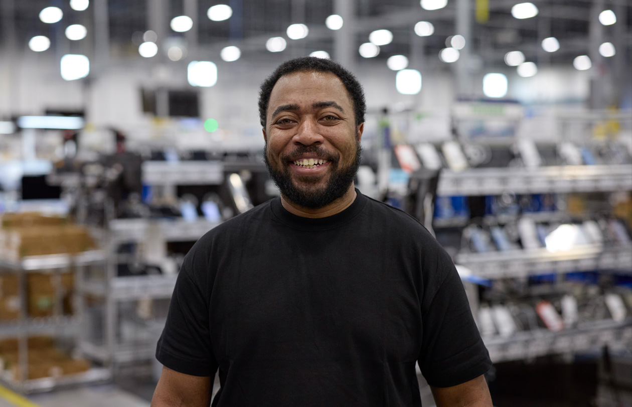 An employee stands in a logistics and repair centre, smiling at the camera