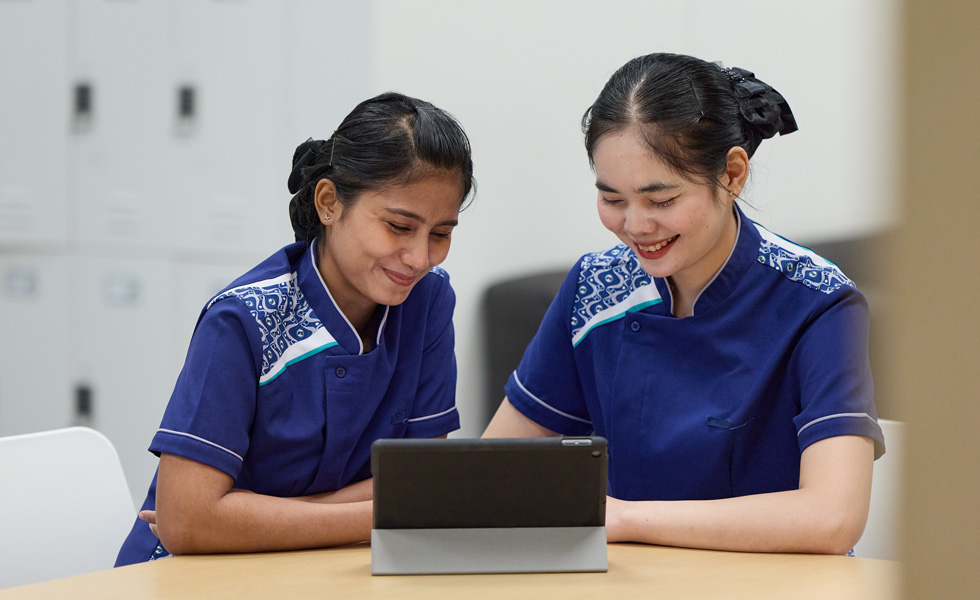 Two uniformed people at a desk share a tablet